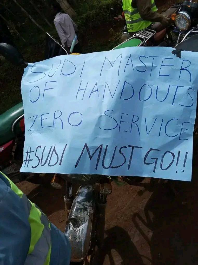 May be an image of 2 people, scooter, motorcycle and text that says 'SUD/ D/ MASTER OF HANDOUTS OUTS ZERO SERVIC #SUDI MUST GO!!'